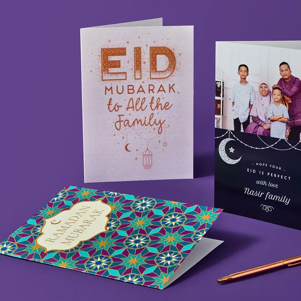 Three Eid and Ramadan greeting cards displayed on a purple surface, including a patterned Ramadan Mubarak card, a glittery Eid Mubarak card, and a personalised card featuring a family photo.